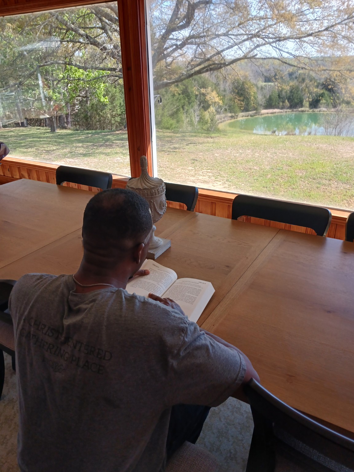 A man reading his Bible at a table overlooking a peaceful pond